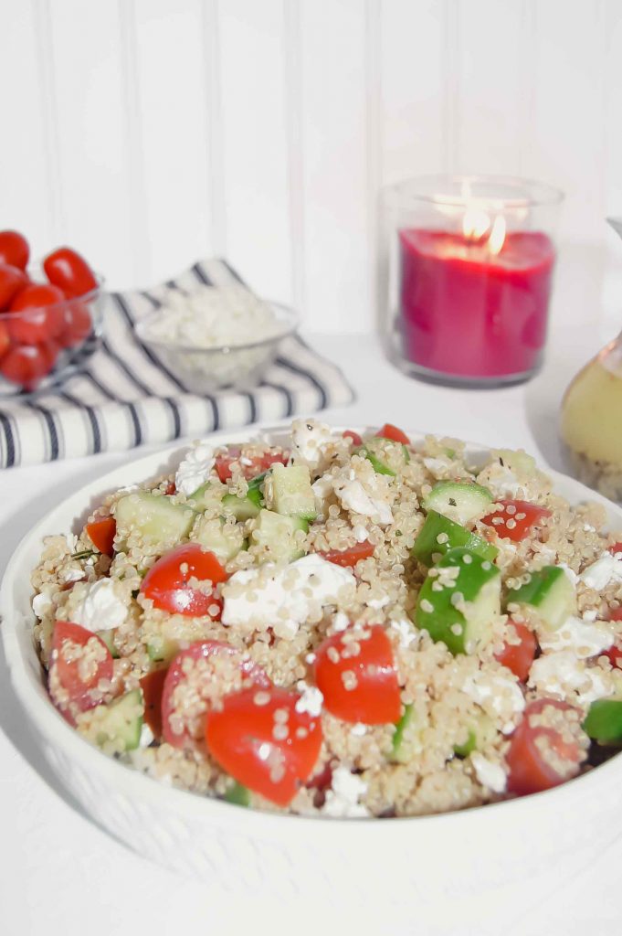 Quinoa Salad with Cucumber, Tomato  and Feta with a bowl of tomatoes and a bowl of feta on a black and white towel, jar of Italian Dressing and candle. www.atwistedplate.com