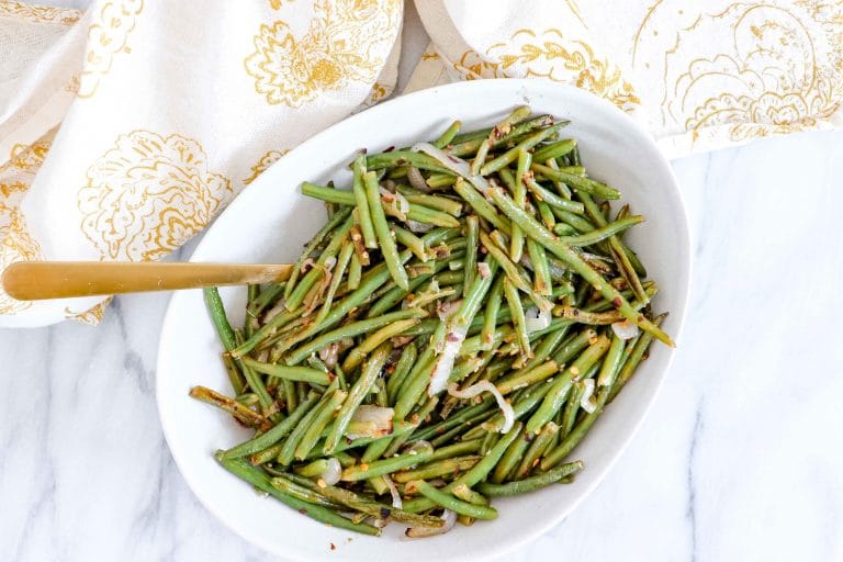 top view of Spicy Green Beans on a round white plate with a gold/white towel. www.atwistedplate.com/spicy-green-beans/