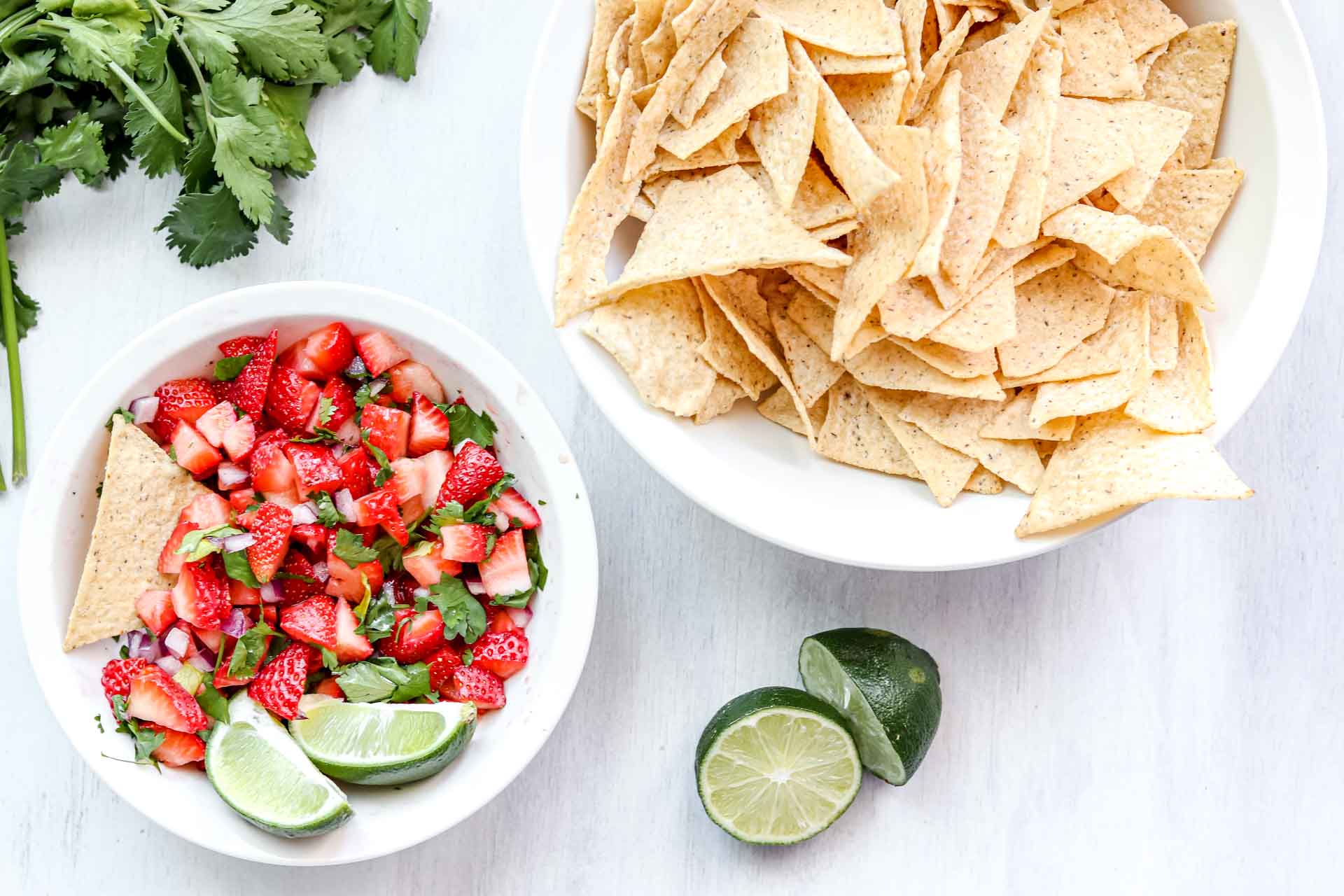 image is a bowl of Strawberry salsa with 2 lime wedges. www.atwistedplate.com/strawberry-salsa/