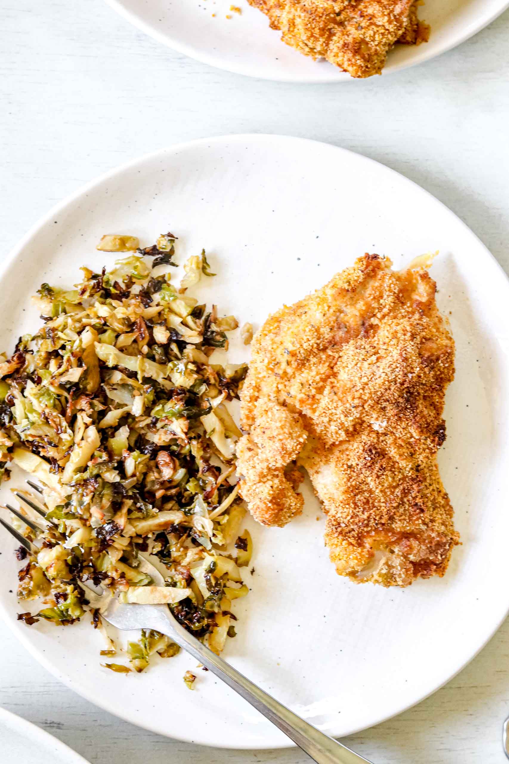Whole 30 Air-fryer Chicken Thigh Almond flour mixture in a bowl. Image of Whole30 Air-fryer  chicken thigh on a round white plate with onion and garlic Brussel sprouts. https://www.atwistedplate.com/whole30-air-fryer-chicken-thighs/